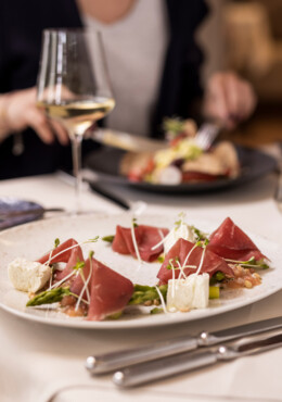 Ein elegantes Gericht mit Schinken, Spargel und Frischkäse auf einem Tisch im Seewirt Mattsee Restaurant, begleitet von Weißwein.