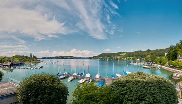 Boote am ruhigen Wasser des Mattsees, umgeben von grüner Landschaft und blühenden Bäumen, mit Blick auf den Seewirt Mattsee.