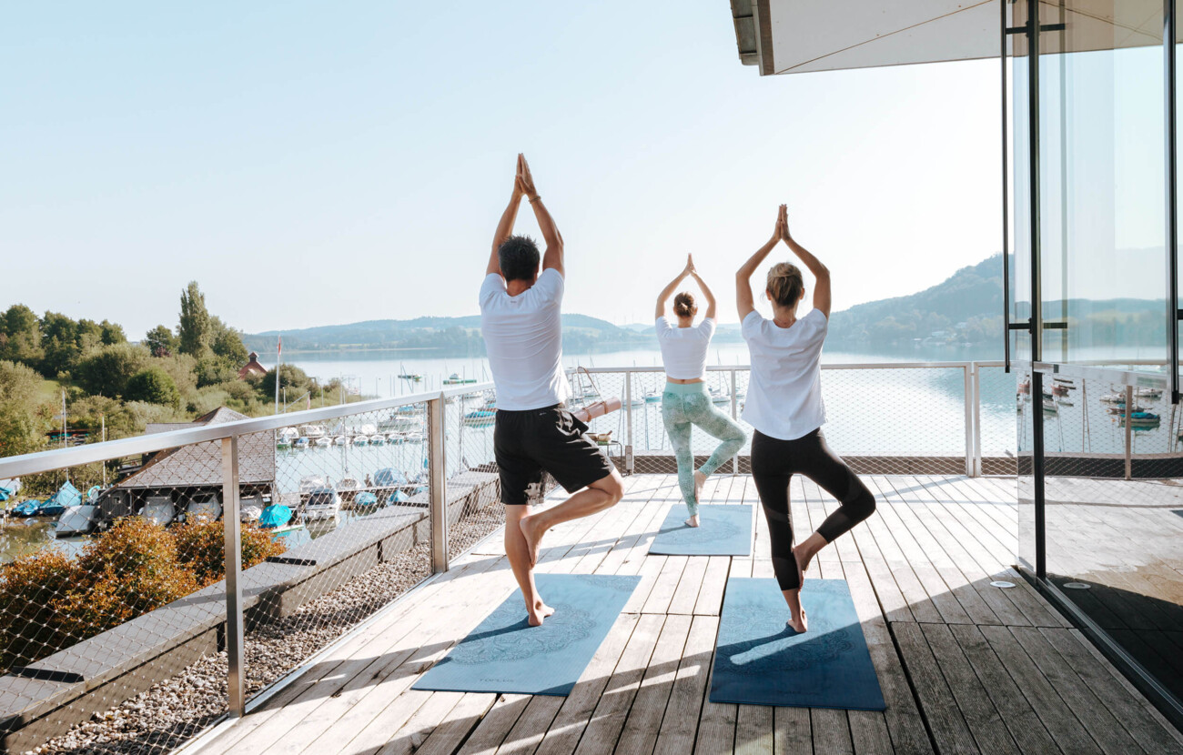 Drei Personen machen Yoga auf einer Terrasse mit Blick auf den See beim Seewirt Mattsee.