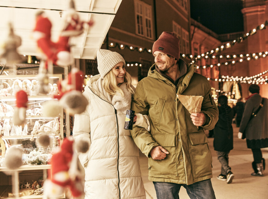 Ein Paar spaziert auf einem Weihnachtsmarkt, umgeben von Lichtern und Dekorationen.