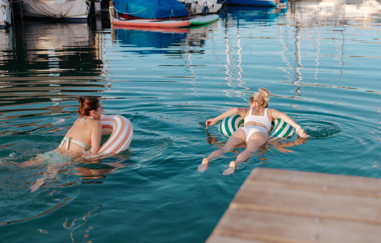 Zwei Frauen schwimmen mit Schwimmringen im Mattsee, umgeben von Booten.