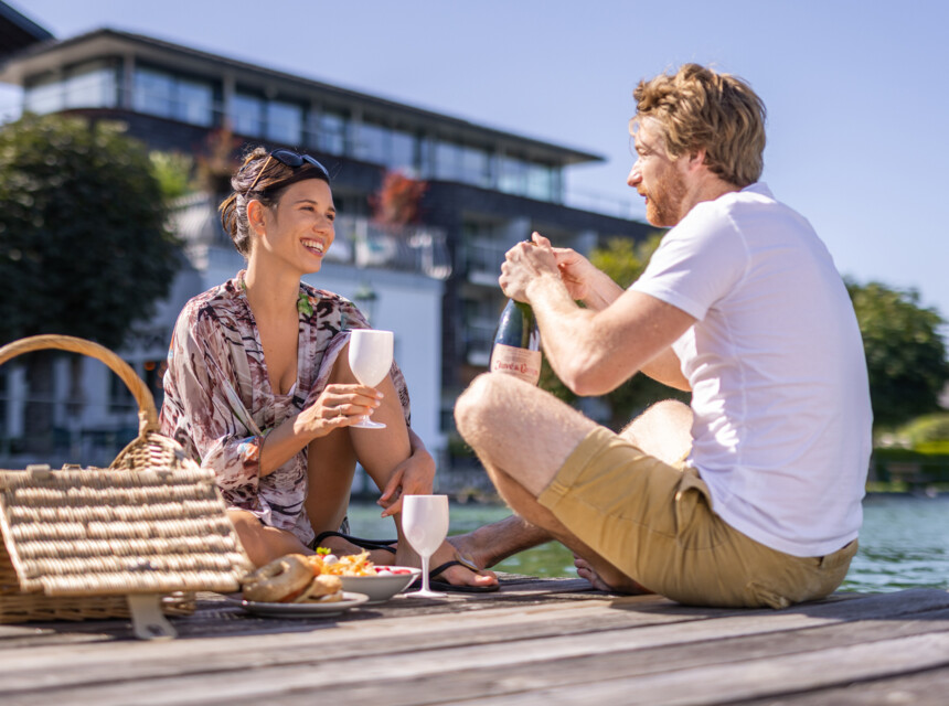 Ein Paar schenkt sich ein Glas Sekt beim Picknick am Steg ein