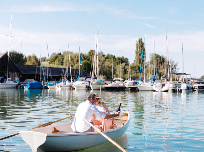 Beim Urlaub am See in Salzburg sitz ein Paar gemeinsam im Ruderboot und öffnet eine Flasche Prosecco