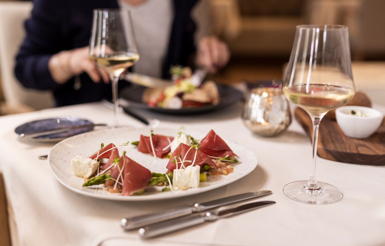 Ein elegantes Gericht mit Schinken, Spargel und Frischkäse auf einem Tisch im Seewirt Mattsee Restaurant, begleitet von Weißwein.
