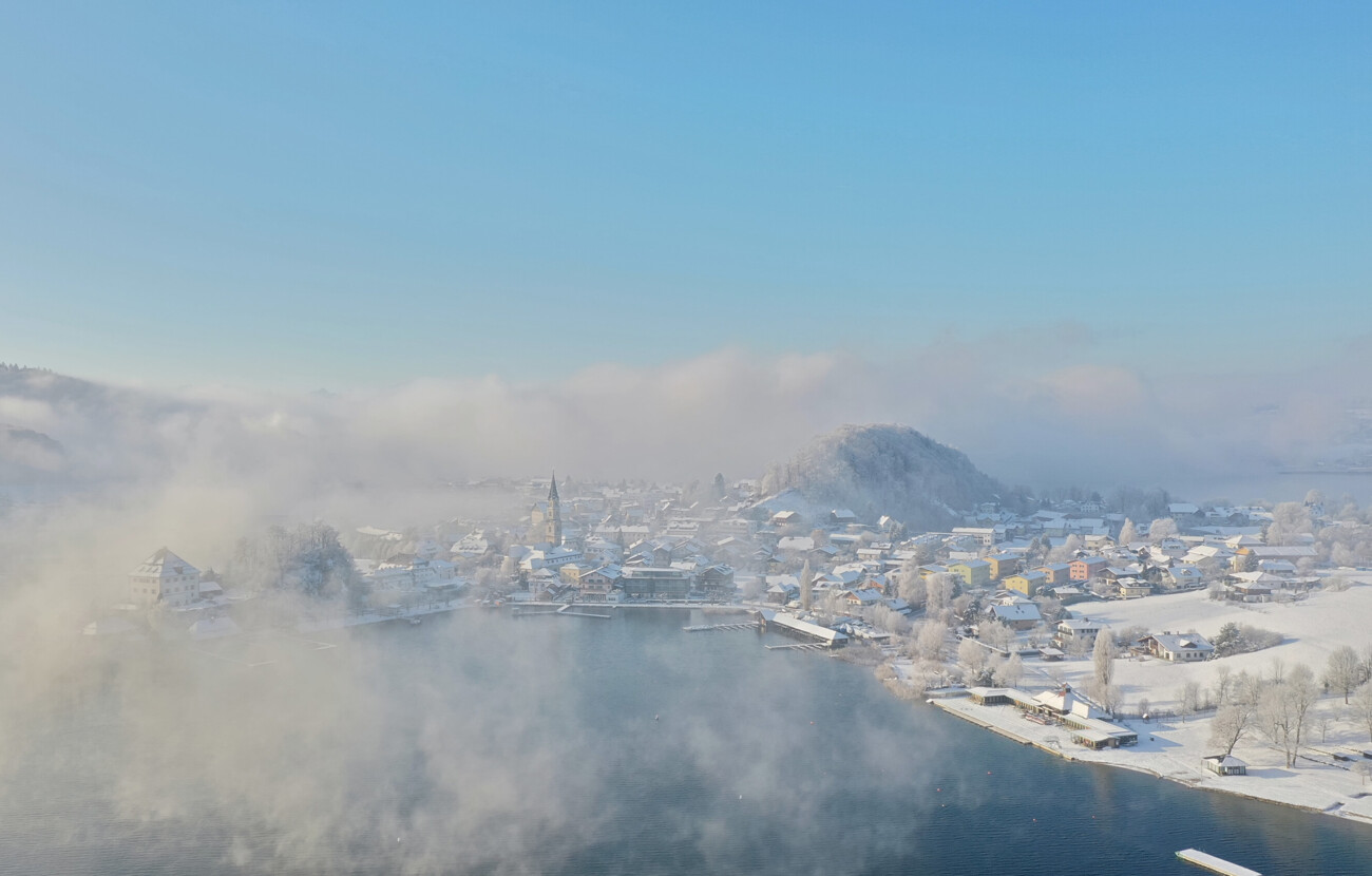 Luftaufnahme von Mattsee im Winter, mit schneebedeckten Häusern und nebligem Himmel, nahe dem Seewirt Mattsee.