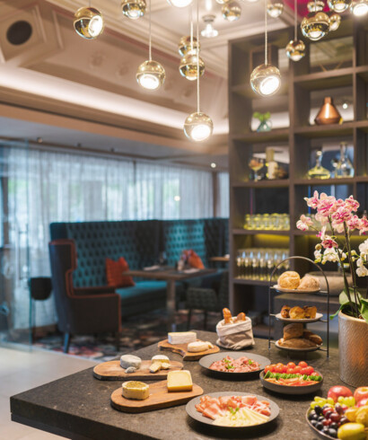 Ein Buffet mit Käse, Wurst, Brot und Obst in einem stilvollen Restaurant im Seewirt Mattsee Hotel. Elegante Beleuchtung und gemütliche Sitzgelegenheiten.