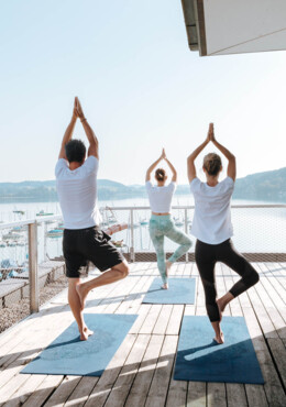 Drei Personen machen Yoga auf einer Terrasse mit Blick auf den See beim Seewirt Mattsee.