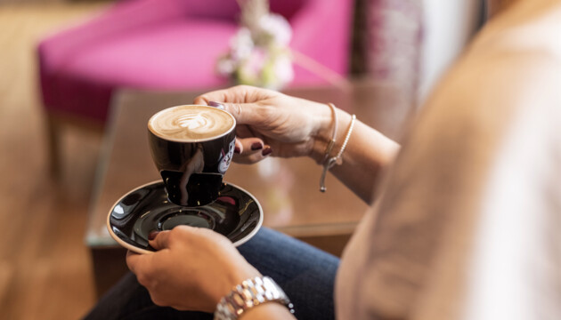 Eine Person hält eine Tasse Cappuccino im gemütlichen Ambiente des Seewirt Mattsee Hotels.