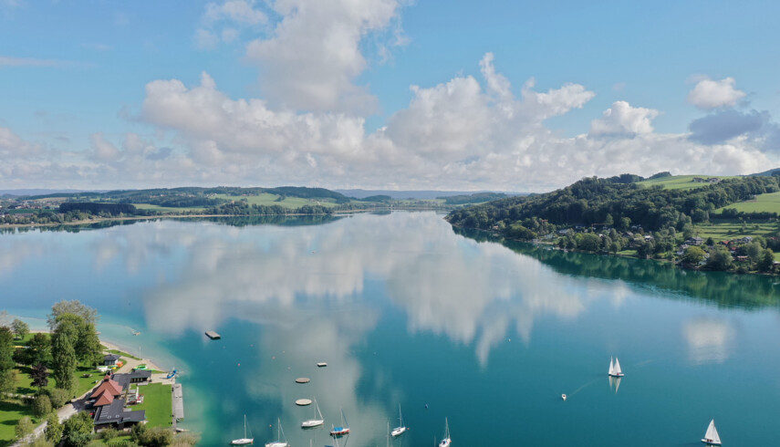 Luftaufnahme des Mattsees mit Segelbooten und bewaldeten Hügeln im Hintergrund, nahe dem Seewirt Mattsee Hotel.