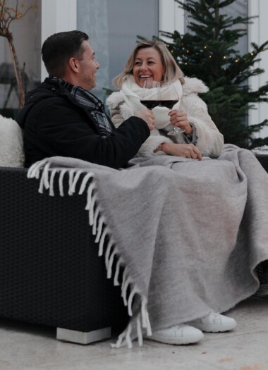 Ein Paar sitzt eingewickelt in Decken mit einem Glas Wein auf der Terrasse