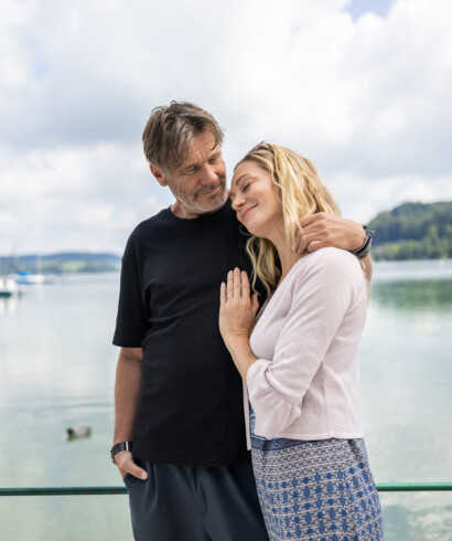 Ein Paar umarmt sich liebevoll vor dem Mattsee mit Booten im Hintergrund.