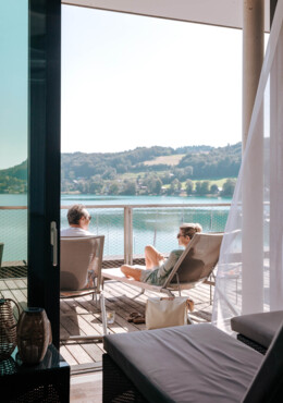 Ein Paar entspannt auf einer Terrasse mit Blick auf den Mattsee, umgeben von grüner Landschaft.