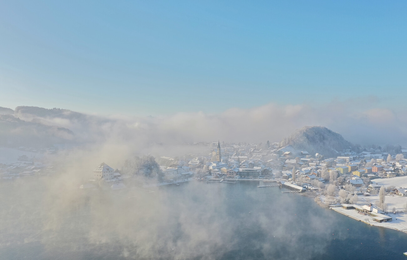 Luftaufnahme von Mattsee im Winter, mit schneebedeckten Häusern und nebligem Himmel, nahe dem Seewirt Mattsee.