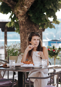 Frau genießt Kaffee und Croissant im Freien, mit Blick auf den See beim Seewirt Mattsee.